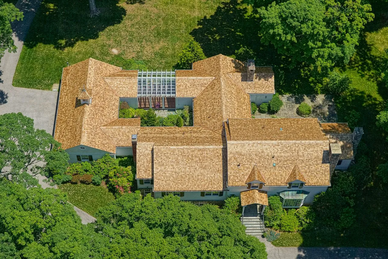 Top-down aerial view of an expansive cedar roof surrounded by mature landscaping